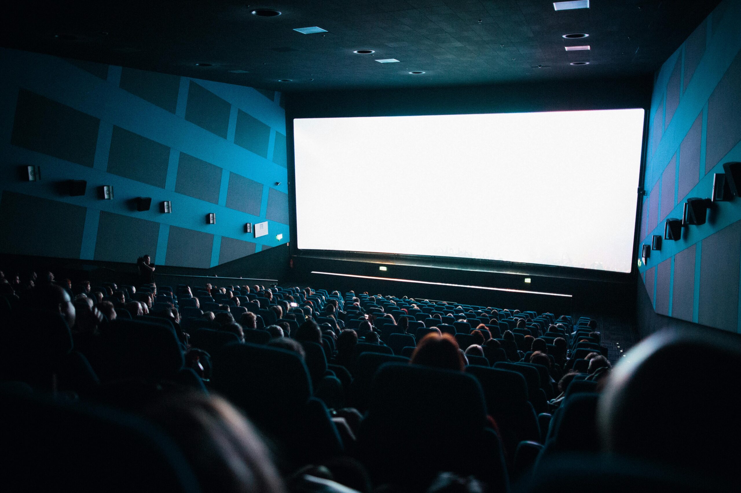 A crowded cinema audience seated in a theater watching a movie on a large screen.