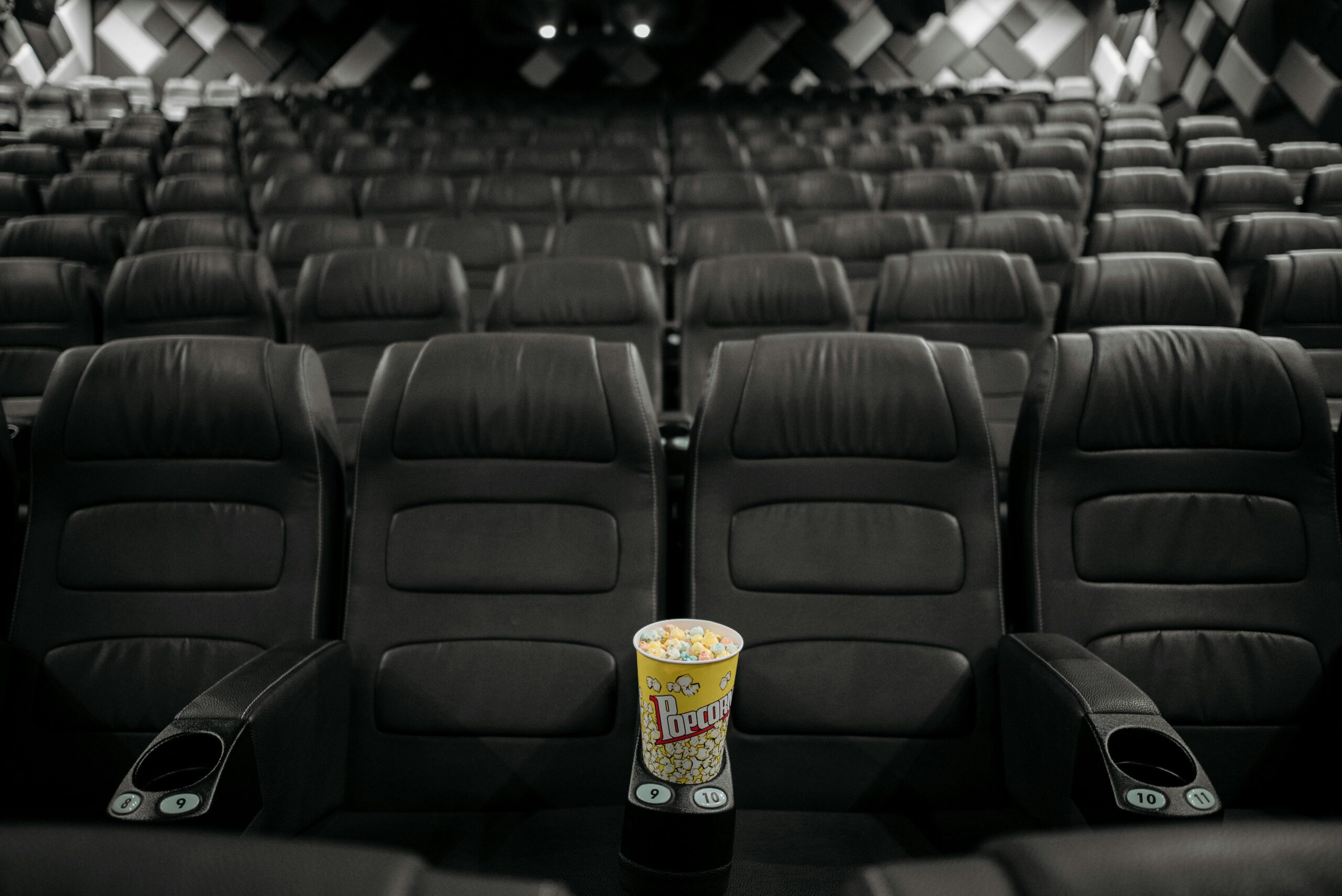 An empty cinema hall with black leather seats and a bucket of popcorn on an armrest.
