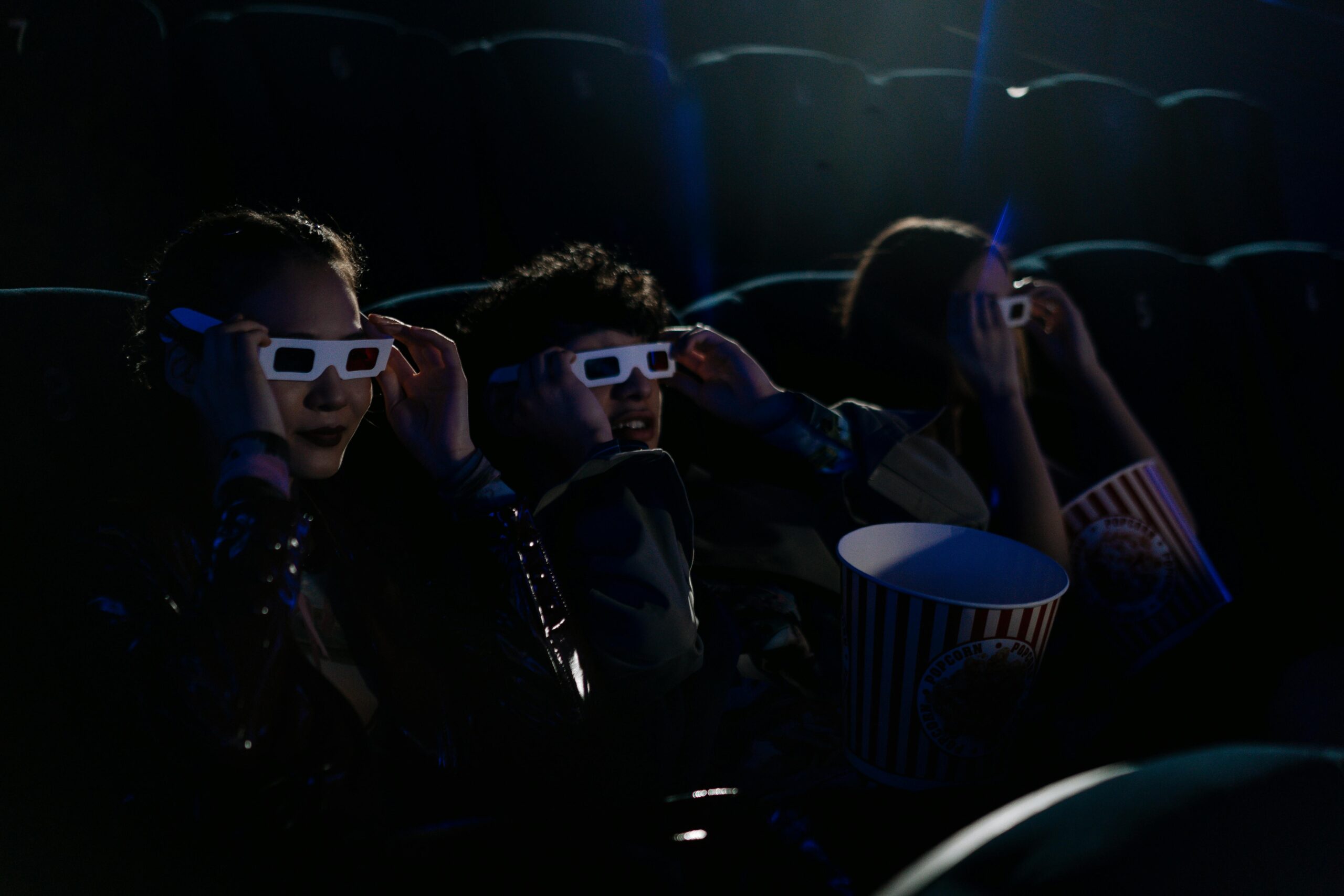 Group of teenagers wearing 3D glasses in a cinema with popcorn during a movie.
